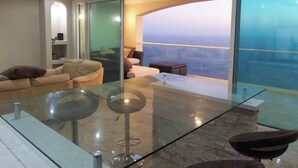 A modern living room with a glass table, a sofa, and a view of the cityscape. - Gorgeous Ocean Front Condo -Rosarito Beach -VIEWS! (Rosarito)
