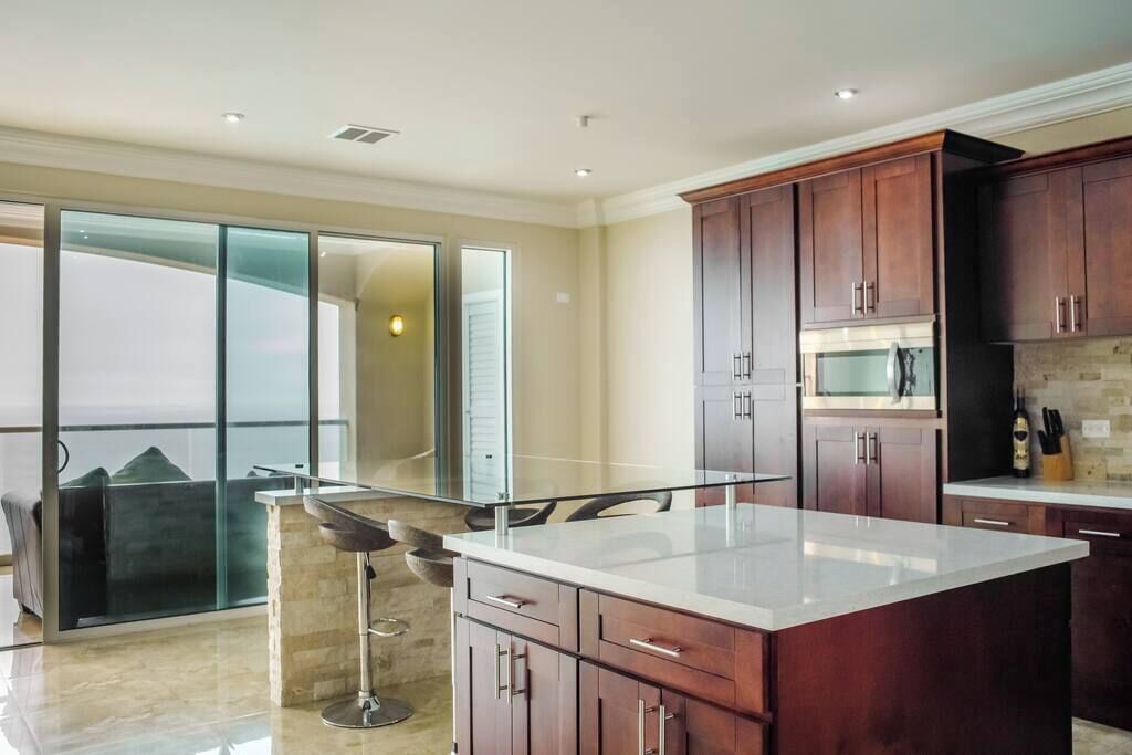 Una cocina moderna con armarios de madera oscura, una isla grande y un área de comedor con paredes de vidrio.