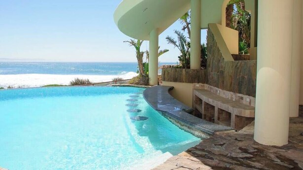 A pool with a curved edge, a stone pathway, and a view of the ocean. - Gorgeous Ocean Front Condo -Rosarito Beach -VIEWS! (Rosarito)