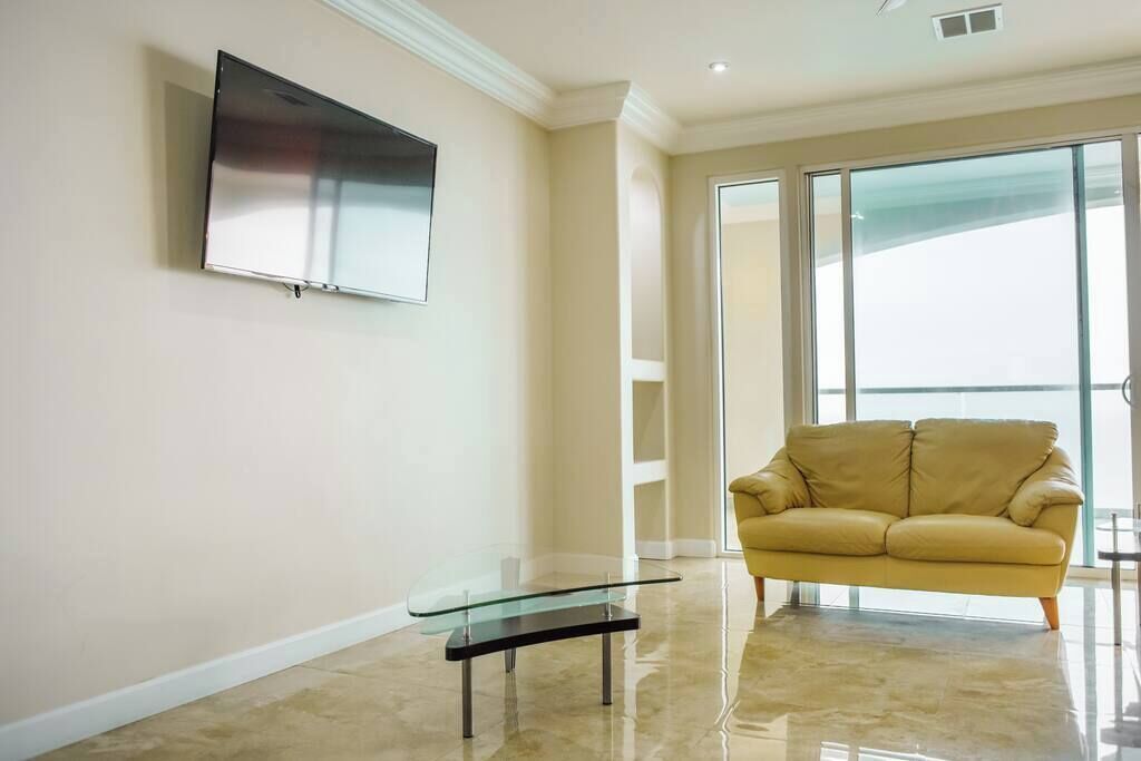 Un salon moderne avec une table basse en verre, un canapé et un téléviseur à écran plat fixé au mur.