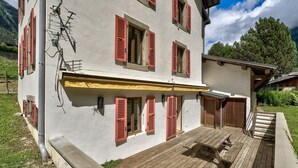 A two-story building with red shutters, a wooden deck, and a yellow awning. - Serenite Spacious 3 Bed Apartment, Chamonix Town (Chamonix-Mont-Blanc)
