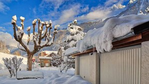 A snow-covered landscape with a building and mountains in the background. - Serenite Spacious 3 Bed Apartment, Chamonix Town (Chamonix-Mont-Blanc)