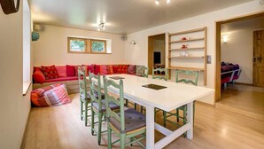 A dining area with a white table, green chairs, and a red sofa with cushions. There are shelves with items on the wall and a door leading to another room. - Serenite Spacious 3 Bed Apartment, Chamonix Town (Chamonix-Mont-Blanc)