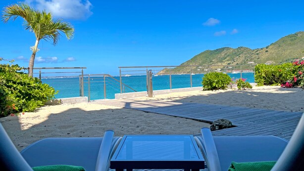 A beachside deck with lounge chairs and a table, overlooking a clear blue sea and a mountainous backdrop. - Grand Case Bleu Marine Sea Side (Grand-Case)