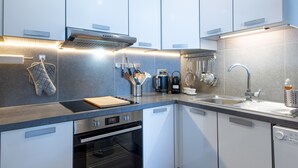 A modern kitchen with white cabinets, stainless steel appliances, and a built-in oven. - Grand Case Bleu Marine Sea Side (Grand-Case)