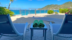 Two lounge chairs with a small table between them, a pair of green towels, and a view of the beach and ocean. - Grand Case Bleu Marine Sea Side (Grand-Case)