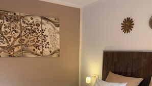 Una cama bien tendida con dos toallas amarillas, un cabecero de madera, una pared con un adorno decorativo y una mesita de noche con una lámpara.