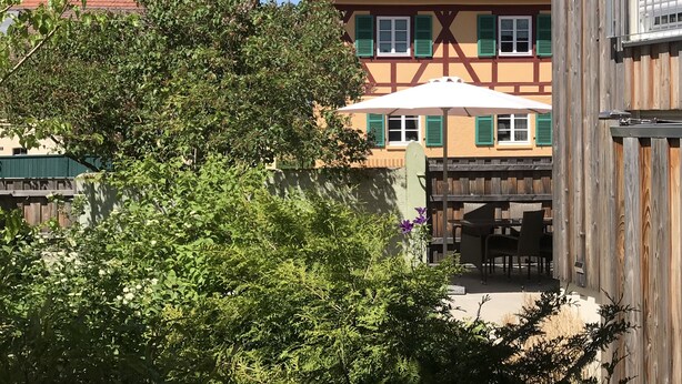 Una casa tradicional de entramado con techo de tejas rojas, contraventanas verdes y una sombrilla blanca sobre una mesa y sillas.