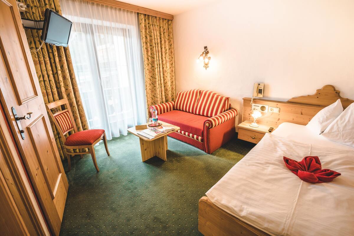 A hotel room with a bed, a sofa, a chair, a small table, a television, and a telephone.