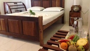 A wooden bed with a white mattress and pillows, a bedside table with a lamp, and a fruit basket on the floor. - Riverston mountain view bungalow (Matale)