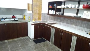 A kitchen with dark wooden cabinets, a gas stove, a sink, and a countertop with shelves holding kitchenware. - Riverston mountain view bungalow (Matale)