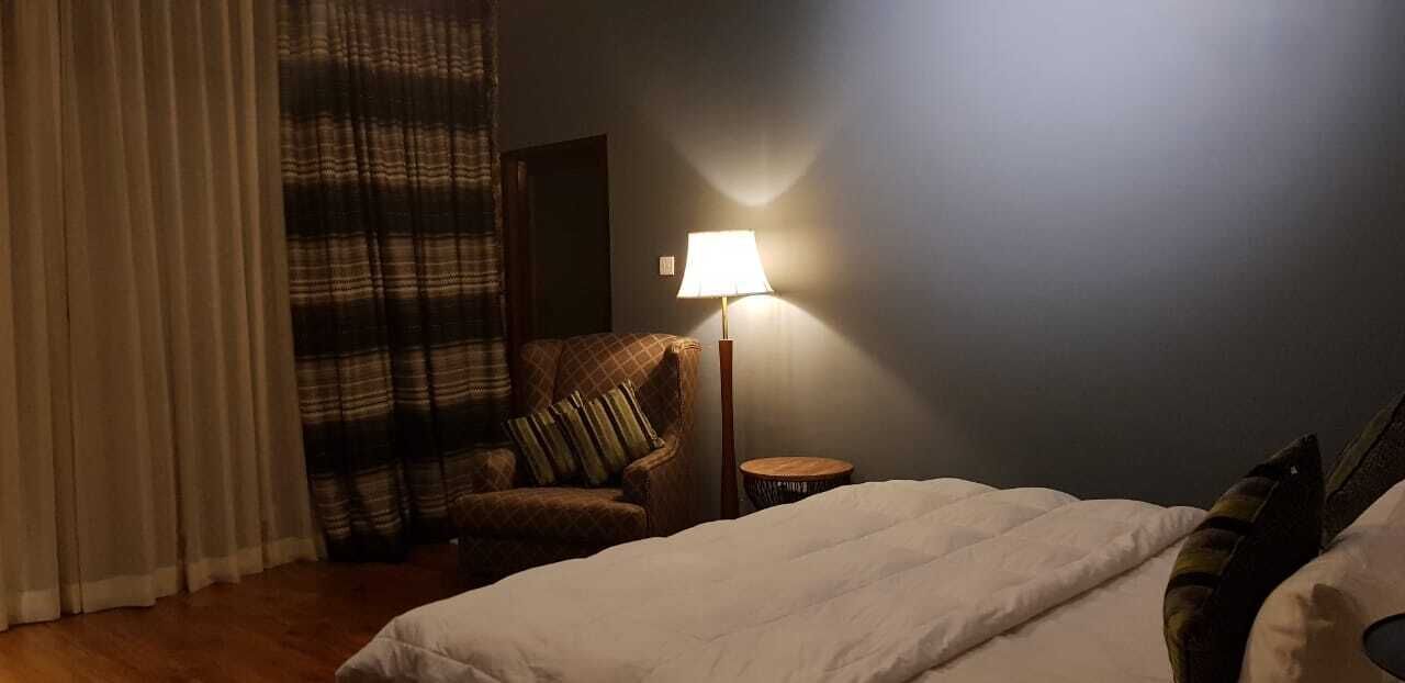 Ein Hotelzimmer mit Bett, Stuhl, Lampe und einem Fenster mit Vorhängen.