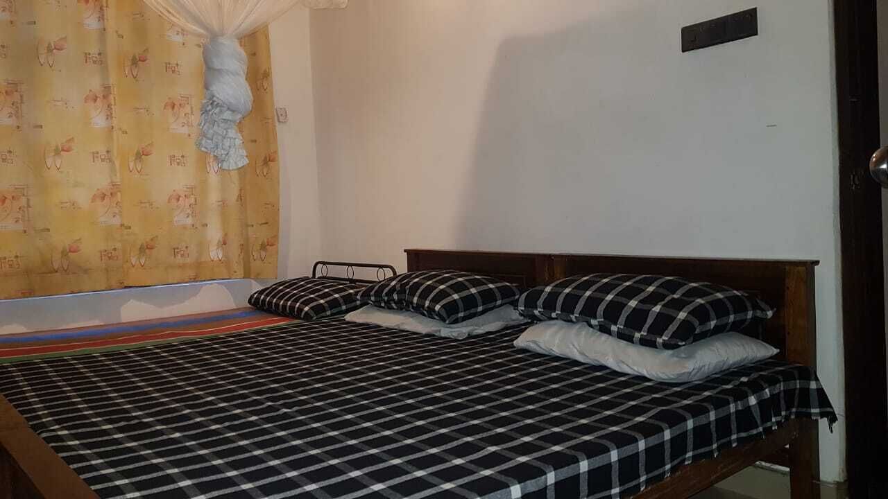 Een enkel bed met een zwart-wit geruit beddegoed en passende kussens, een klamboe en een geel gordijn met een fruitprint.