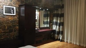 A room with a stone wall, a wooden floor, a dark wooden cabinet, a mirror, and a window with striped curtains. - Riverston mountain view bungalow (Matale)