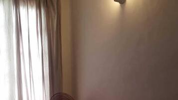 A dimly lit room with a bed, a standing fan, and a wall-mounted light fixture.