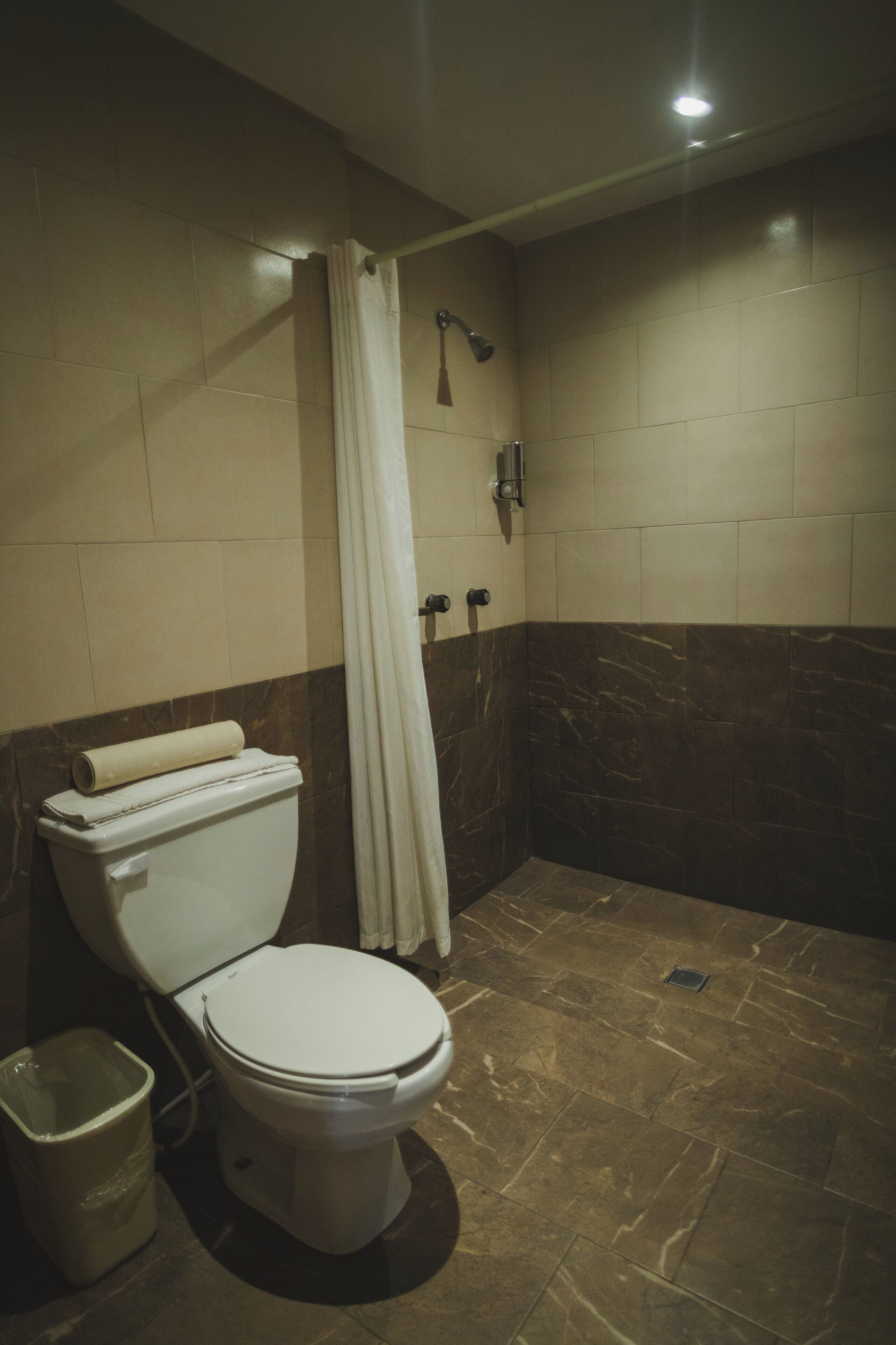 A bathroom with a toilet, a shower curtain, and a trash bin.