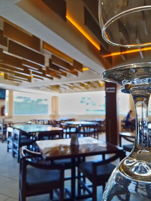 A restaurant interior with tables and chairs, a large window, and a decorative glass structure. - Hotel Villa Esmeralda (San Juan Bautista Tuxtepec)