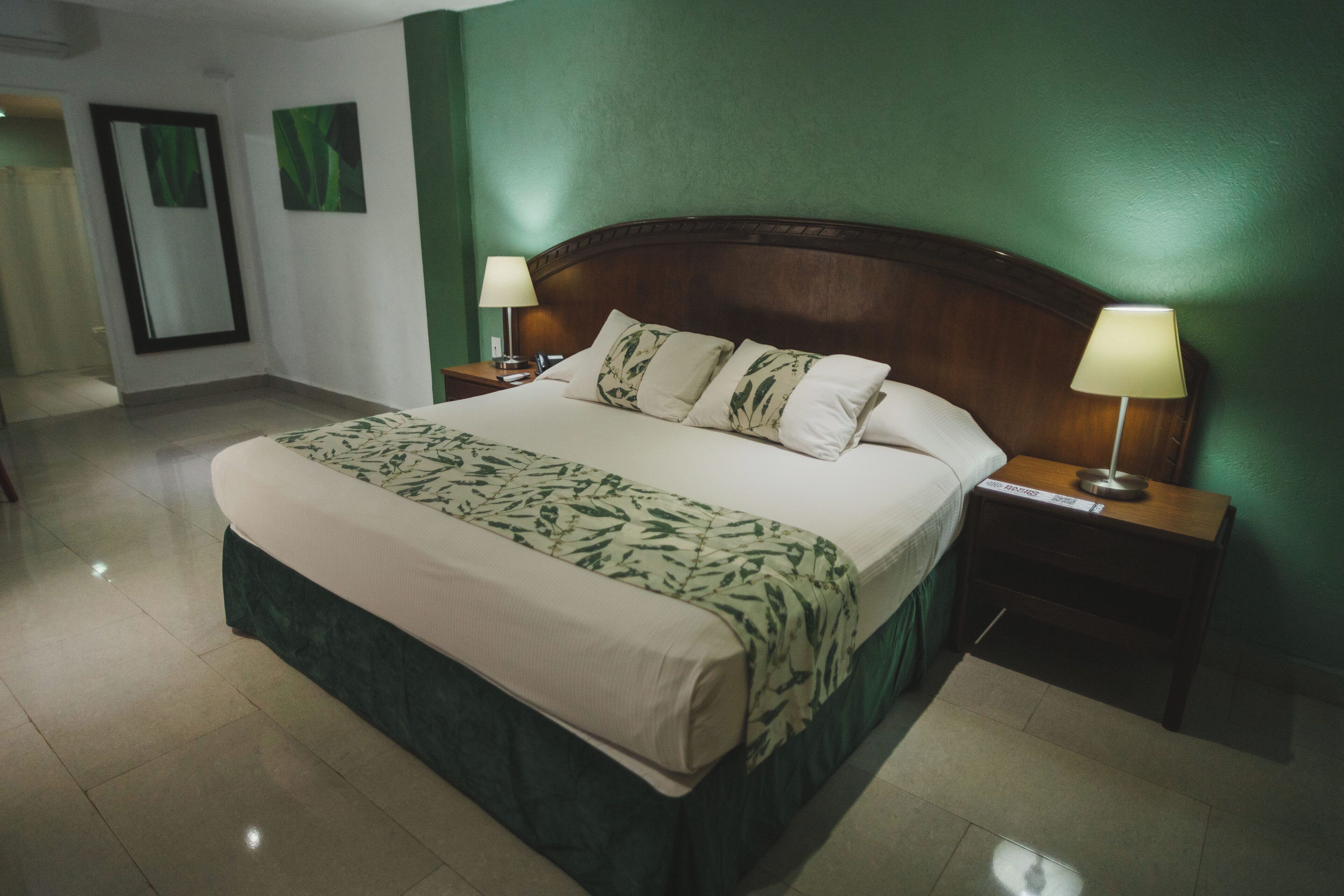 A hotel room with a large bed, two bedside tables with lamps, a green wall, and a mirror.