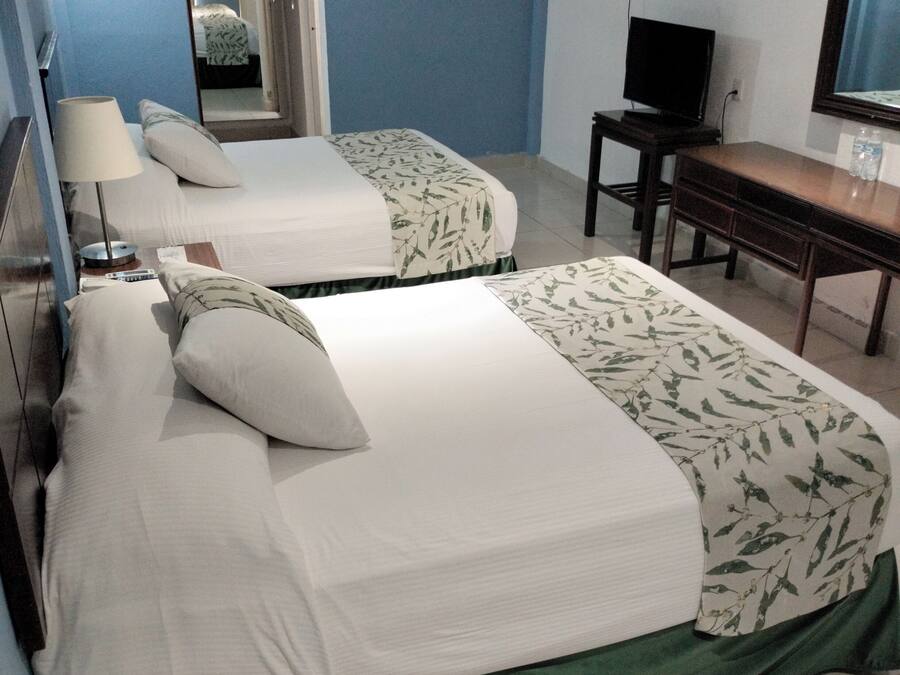 A hotel room with two beds, a desk, a television, and an air conditioning unit.