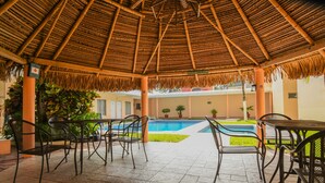 Un área de estar al aire libre con techo de paja, piscina y plantas en macetas.