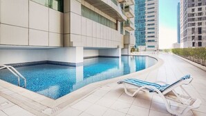 A swimming pool with a tiled deck, a lounge chair, and modern buildings in the background. - DM1 Comfortable Apartment in Dubai Marina (Dubai)