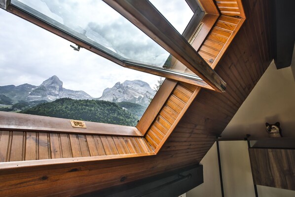 Habitación con techo inclinado y tragaluces, con vistas a una cordillera.