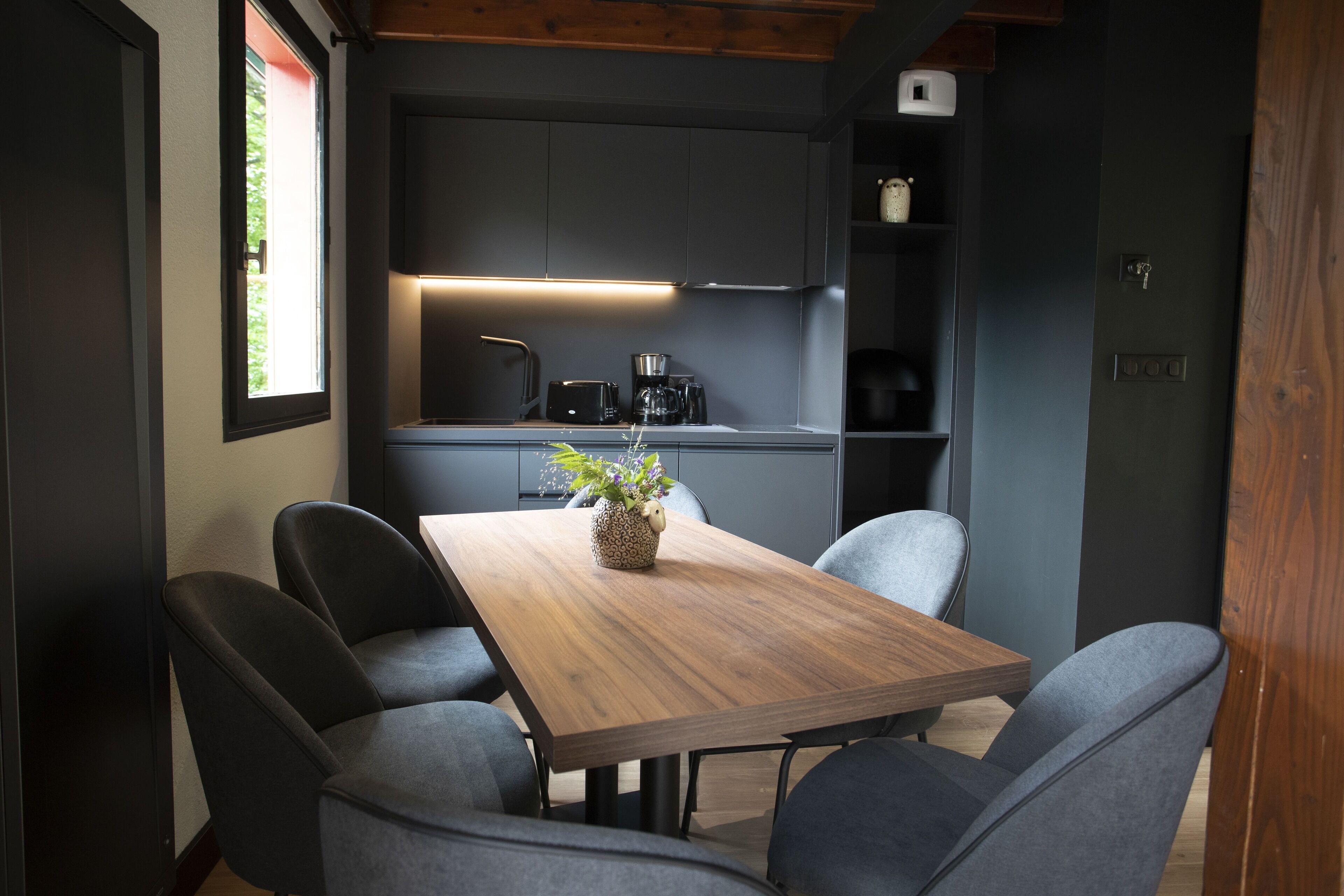 Eine moderne Küche mit dunklen Schränken, einem Holztisch und grauen Stühlen.