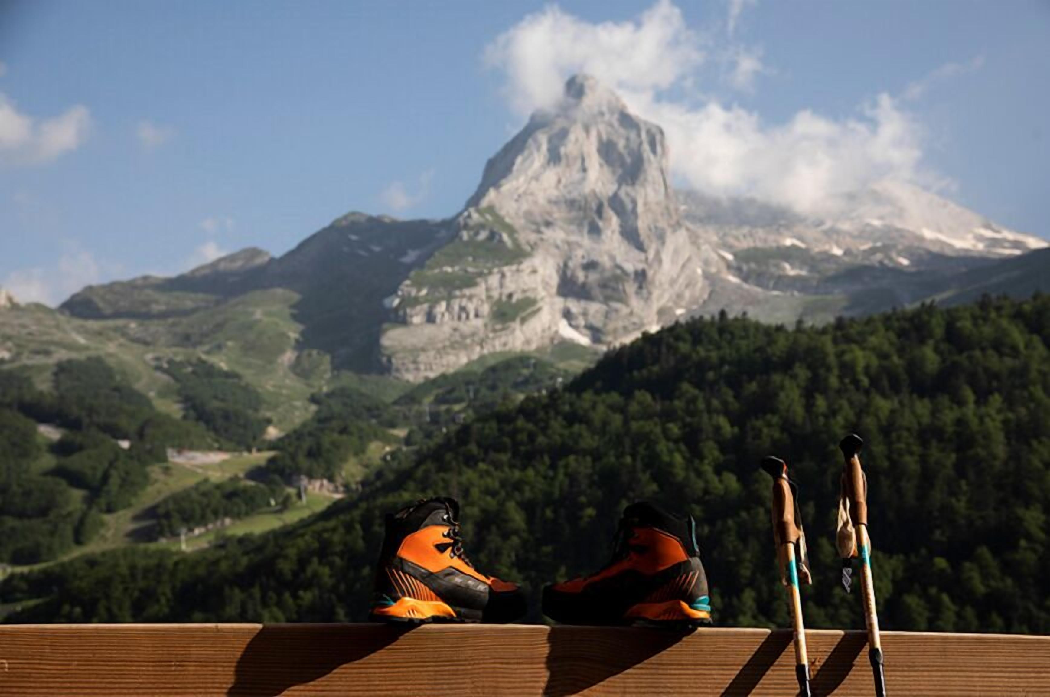 A wooden deck with a pair of orange and black hiking boots and a pair of skis.