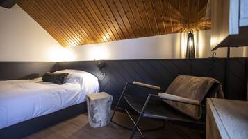 Una habitación moderna con una cama, techo de madera, un taburete pequeño y una silla plegable.