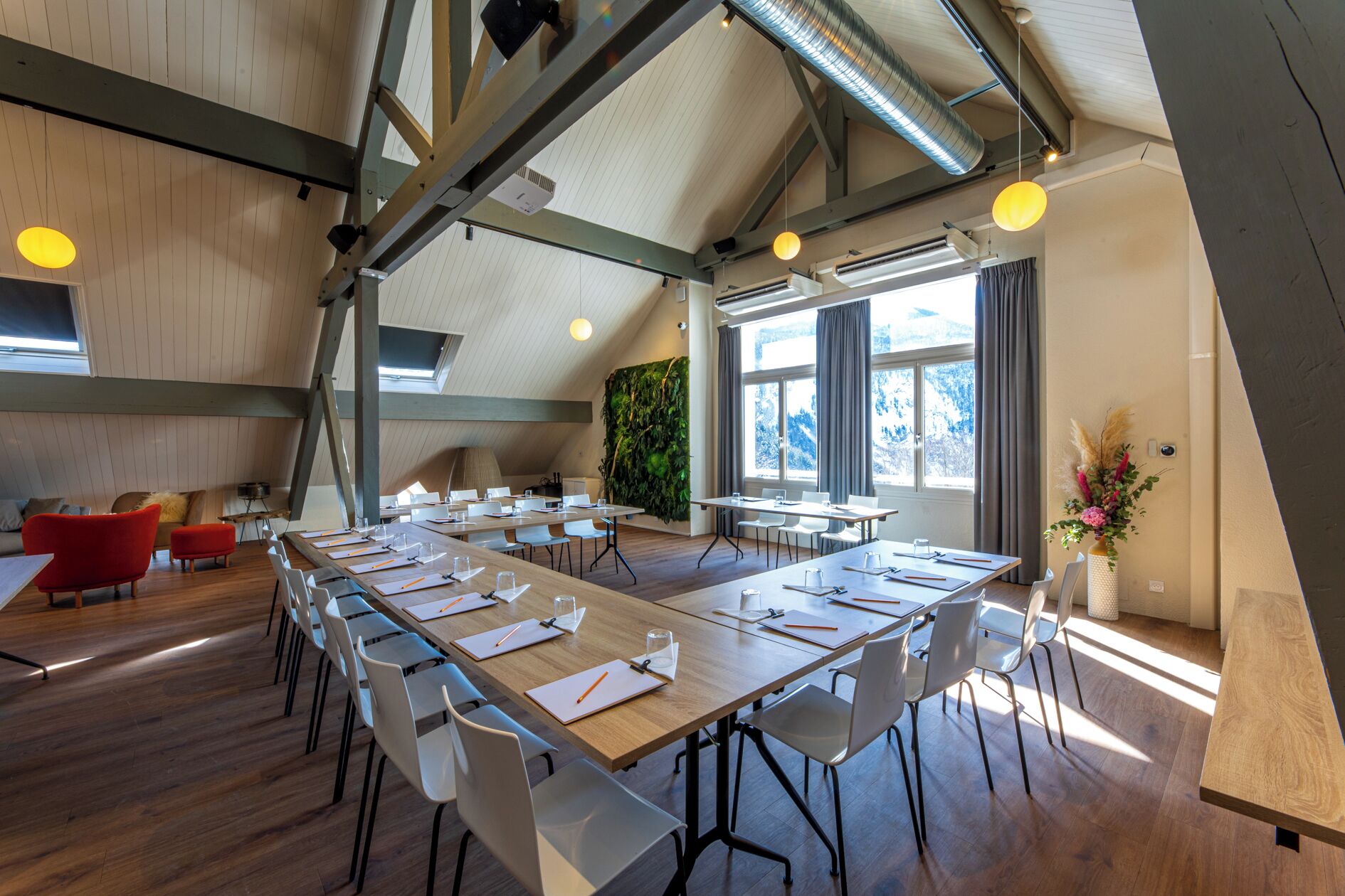 Une salle de conférence moderne, dotée de longues tables, de chaises blanches et d’un plancher en bois.