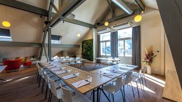 Une salle de conférence moderne, dotée de longues tables, de chaises blanches et d’un plancher en bois.