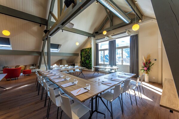 A modern conference room with long tables, white chairs, and a wooden floor.