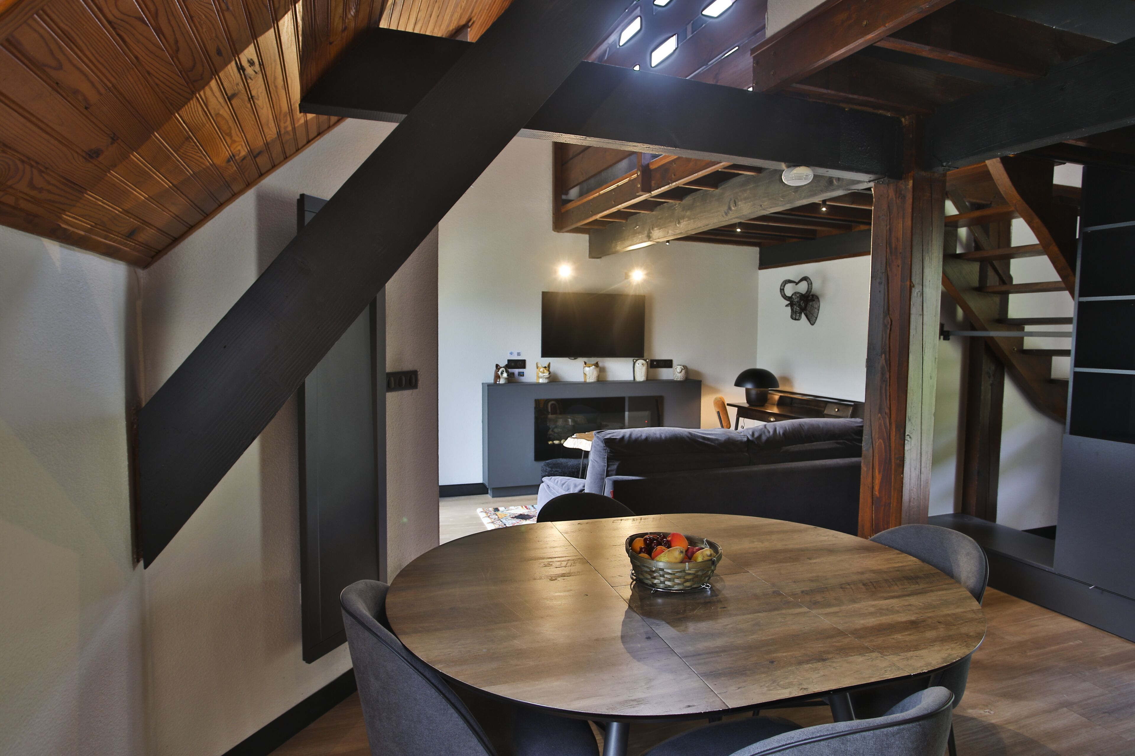 Un interior moderno con una mesa redonda de madera, sillas tapizadas en gris y techo de madera.