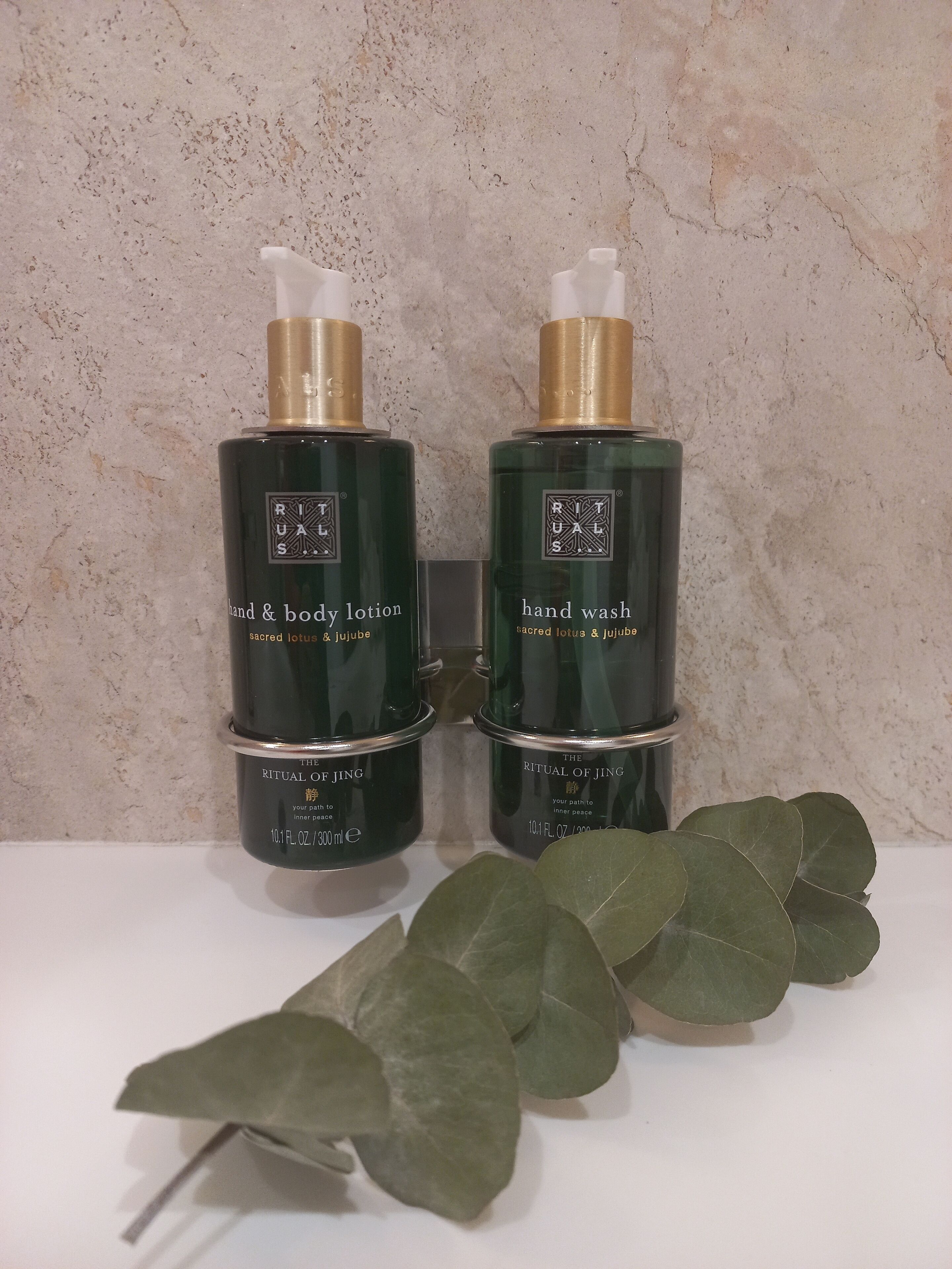 Two bottles of hand and body lotion and hand wash on a white surface with a textured wall in the background.
