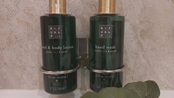 Two bottles of hand and body lotion and hand wash on a white surface with a textured wall in the background.
