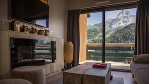 A modern living room with a fireplace, a large window with a mountain view, and a cozy seating area. - ISKÖ Chalets Hotel (Eaux-Bonnes)