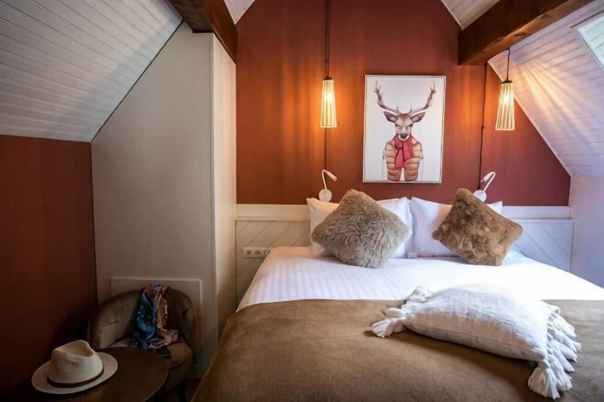 Een slaapkamer met een bed, kussens, een hoed en een schilderij aan de muur.
