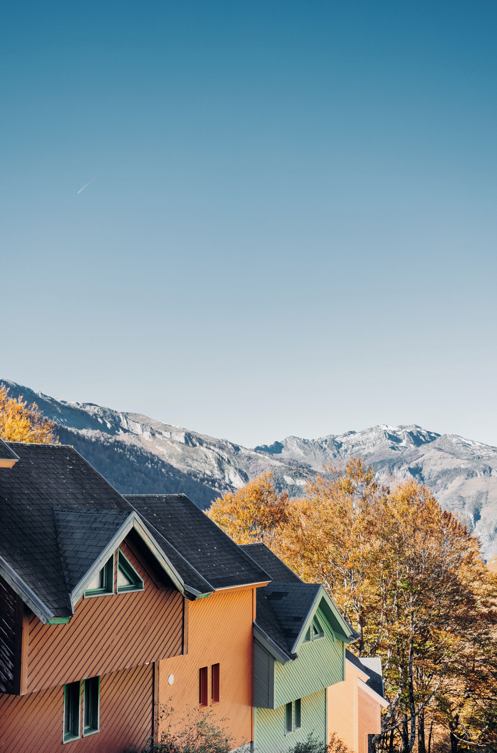 A modern house with a sloped roof, a wooden exterior, and a view of a mountain range.