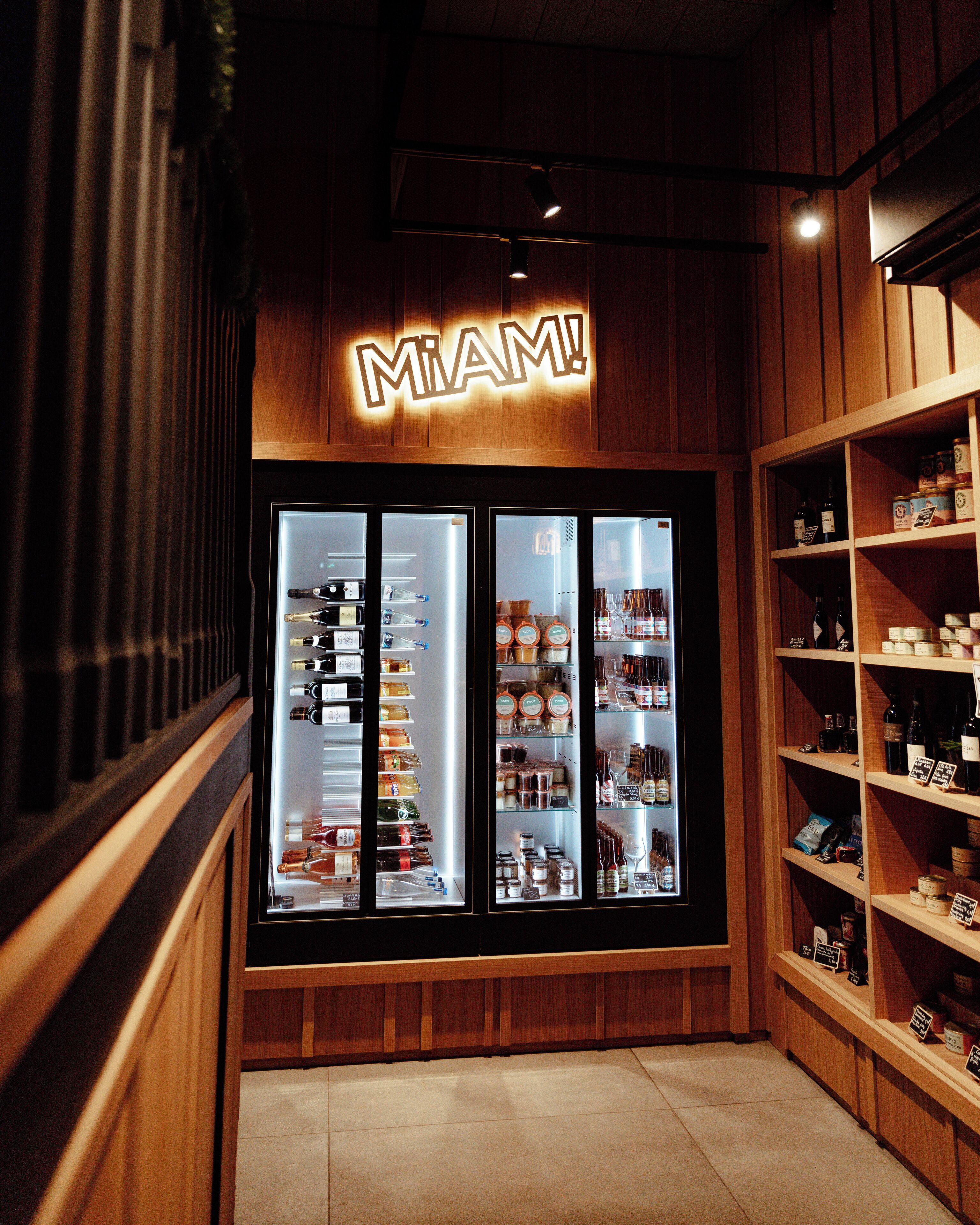 Una tienda con un letrero que dice 'MIAMI!', vitrinas refrigeradas y estantes llenos de diferentes productos.