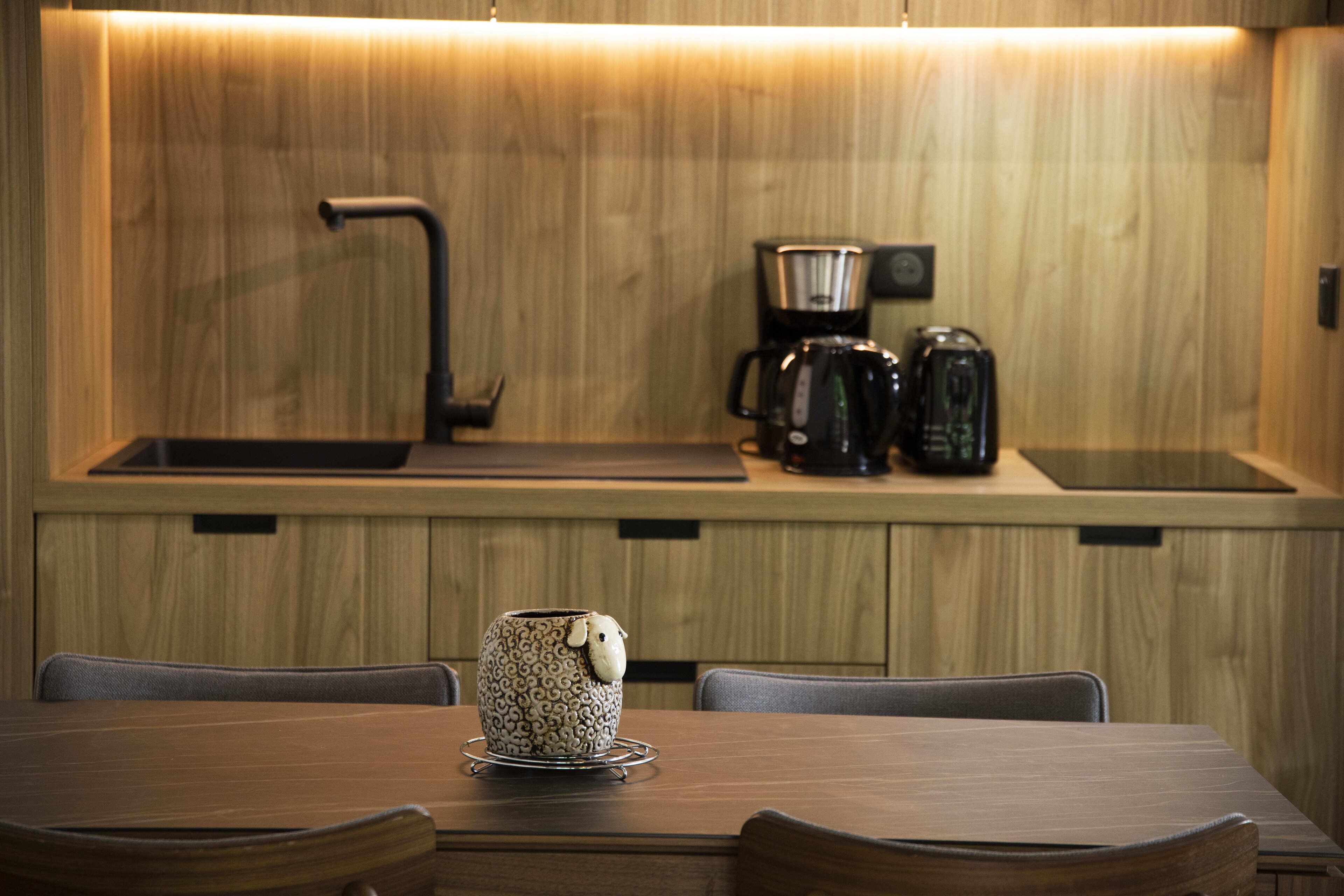Een moderne keuken met houten keukenkastjes, een koffiezetapparaat en een decoratieve keramische beker op het aanrecht.