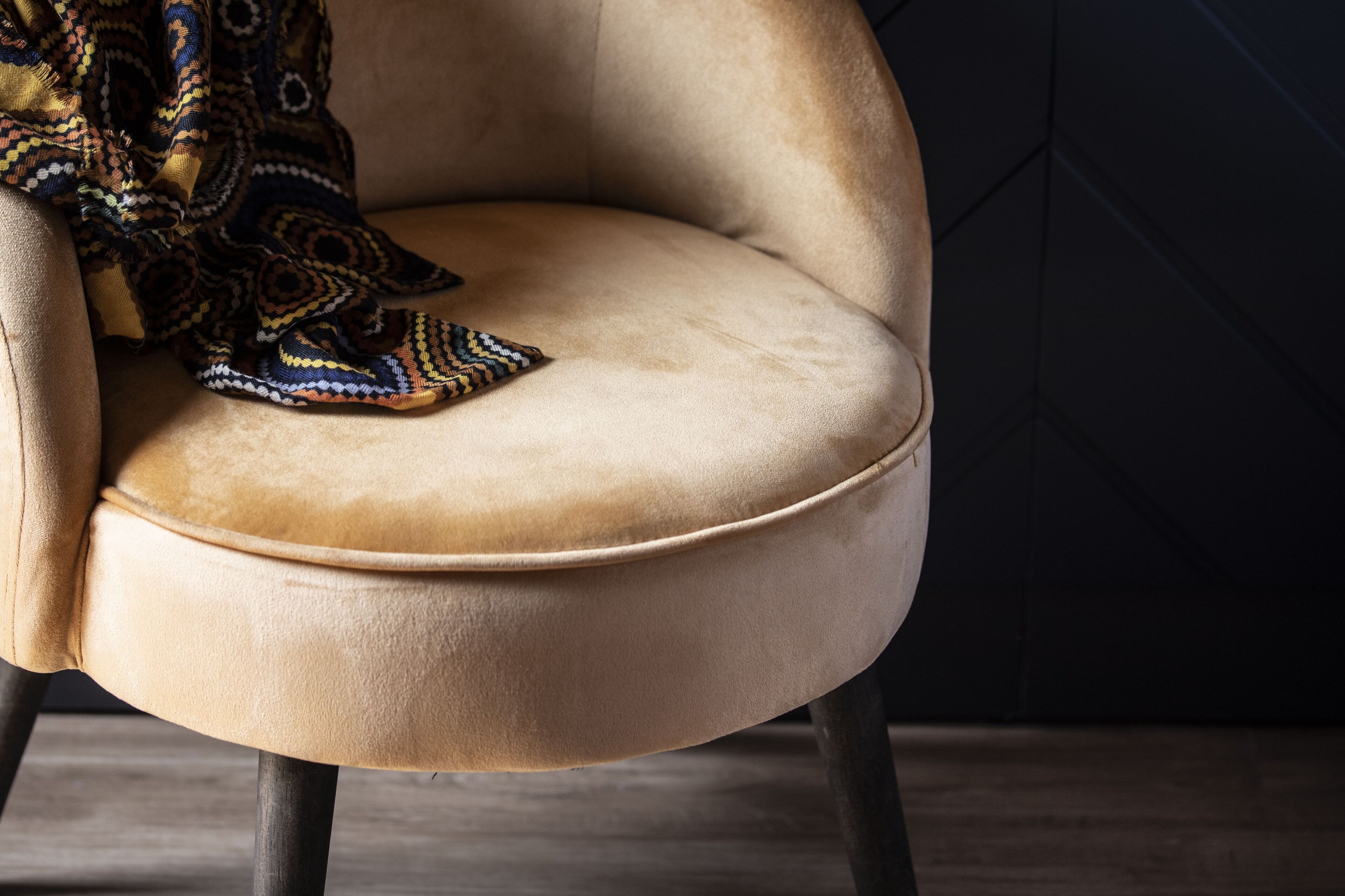 A close-up of a beige upholstered chair with a patterned throw blanket draped over it.