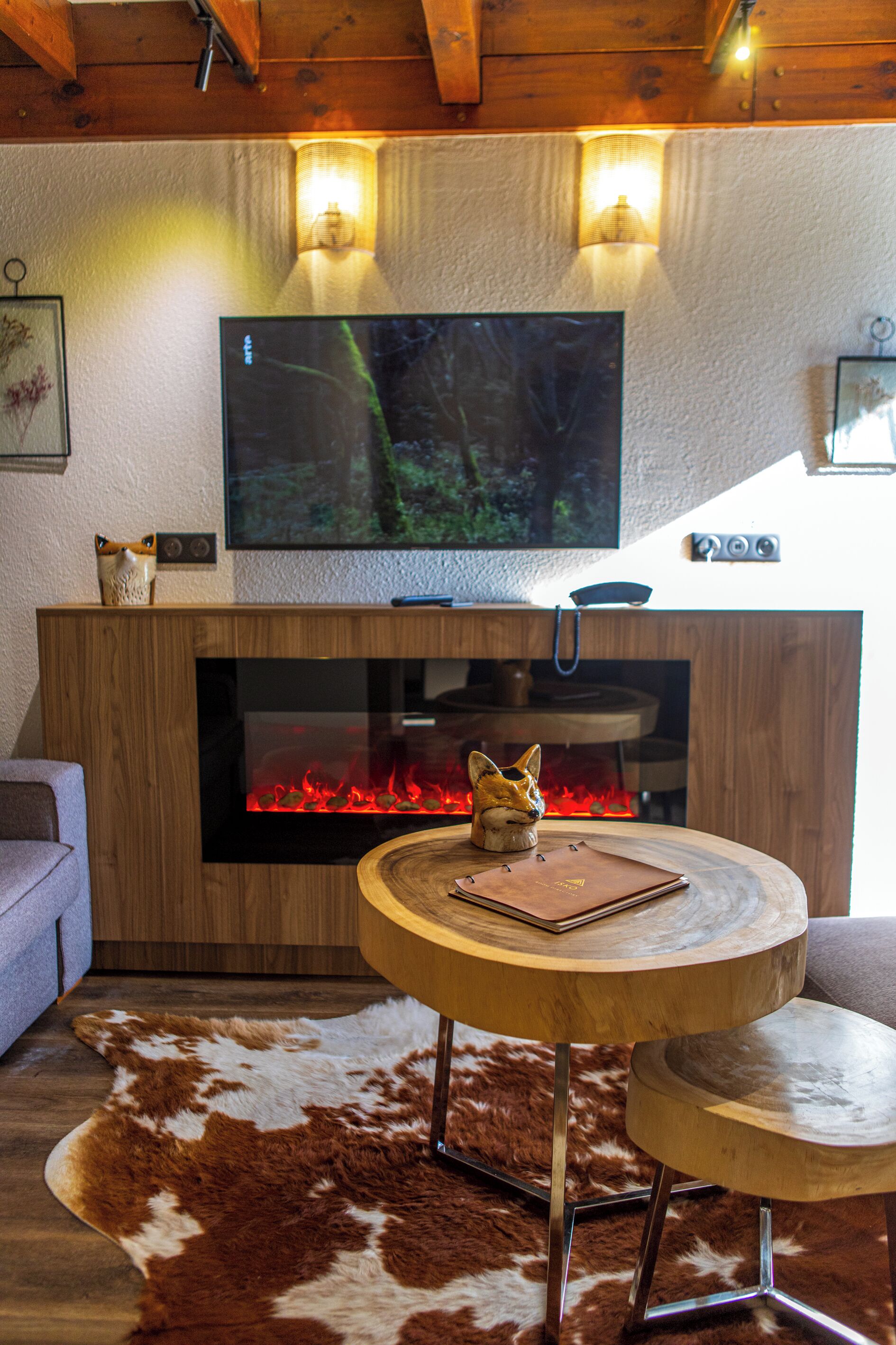 Ein modernes Wohnzimmer mit Kamin, einem an der Wand befestigten Fernseher und einem runden Holztisch mit einem Leder Notizbuch.