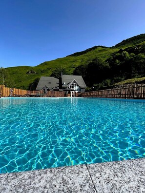 A swimming pool with clear blue water, surrounded by a wooden fence, and a house with a dark roof in the background.