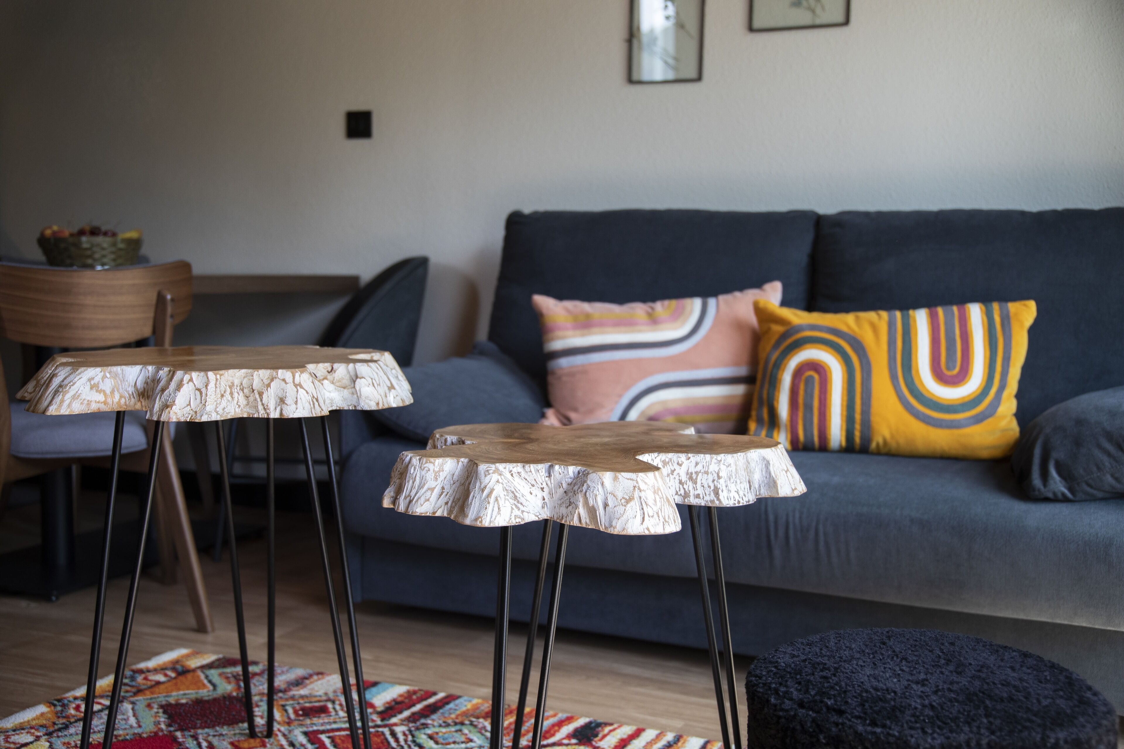 A modern living room with a grey sofa, two wooden tables, and a colorful rug.