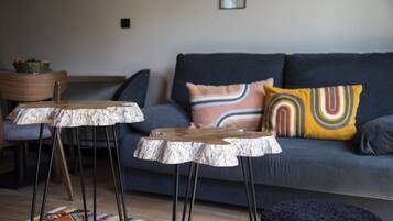 A modern living room with a grey sofa, two wooden tables, and a colorful rug.