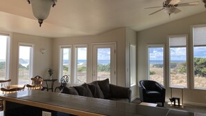 Ein geräumiges Wohnzimmer mit einer großen Kücheninsel, Deckenventilator und Meerblick durch mehrere Fenster.