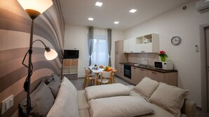 Un espacio habitable compacto con sofá, una mesa de comedor con sillas, una kitchenette y un televisor al fondo.