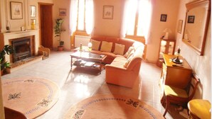 A cozy living room with a fireplace, a sofa, a coffee table, and a dining table. - Inviting 6-Bed Farmhouse (Cravans)