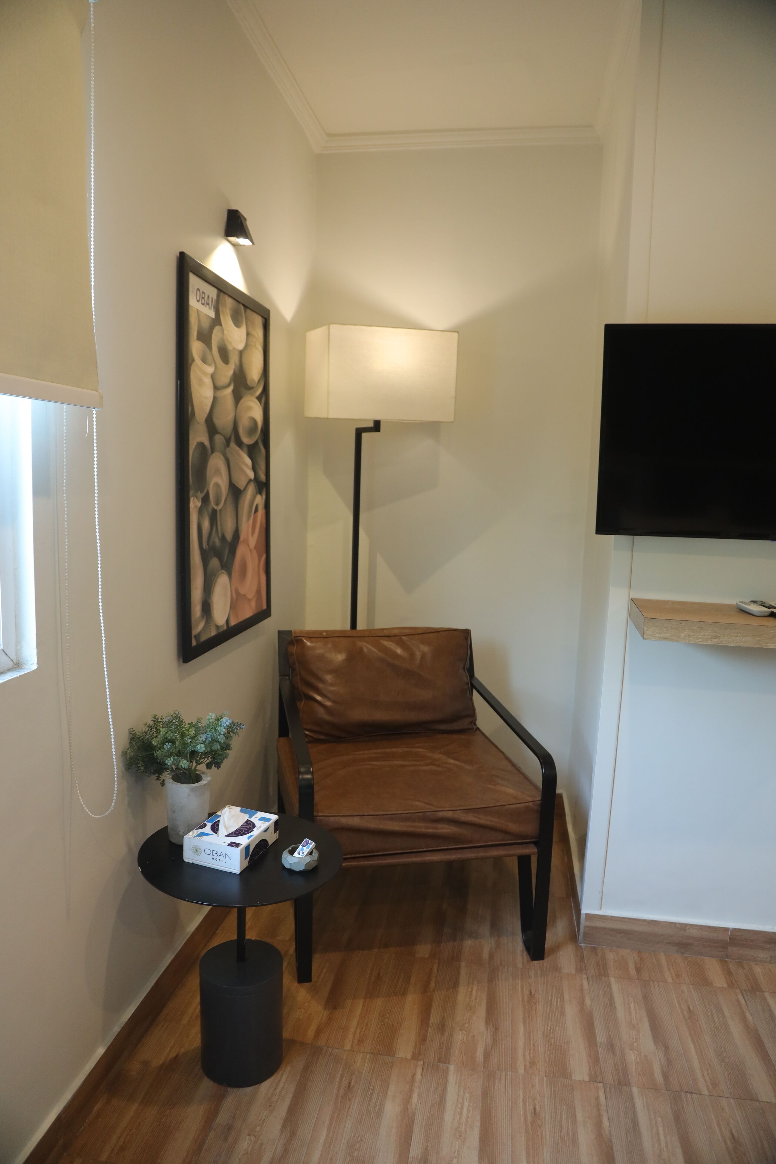 A small room with a brown leather chair, a round table with a lamp, a framed picture on the wall, and a TV mounted on the wall.