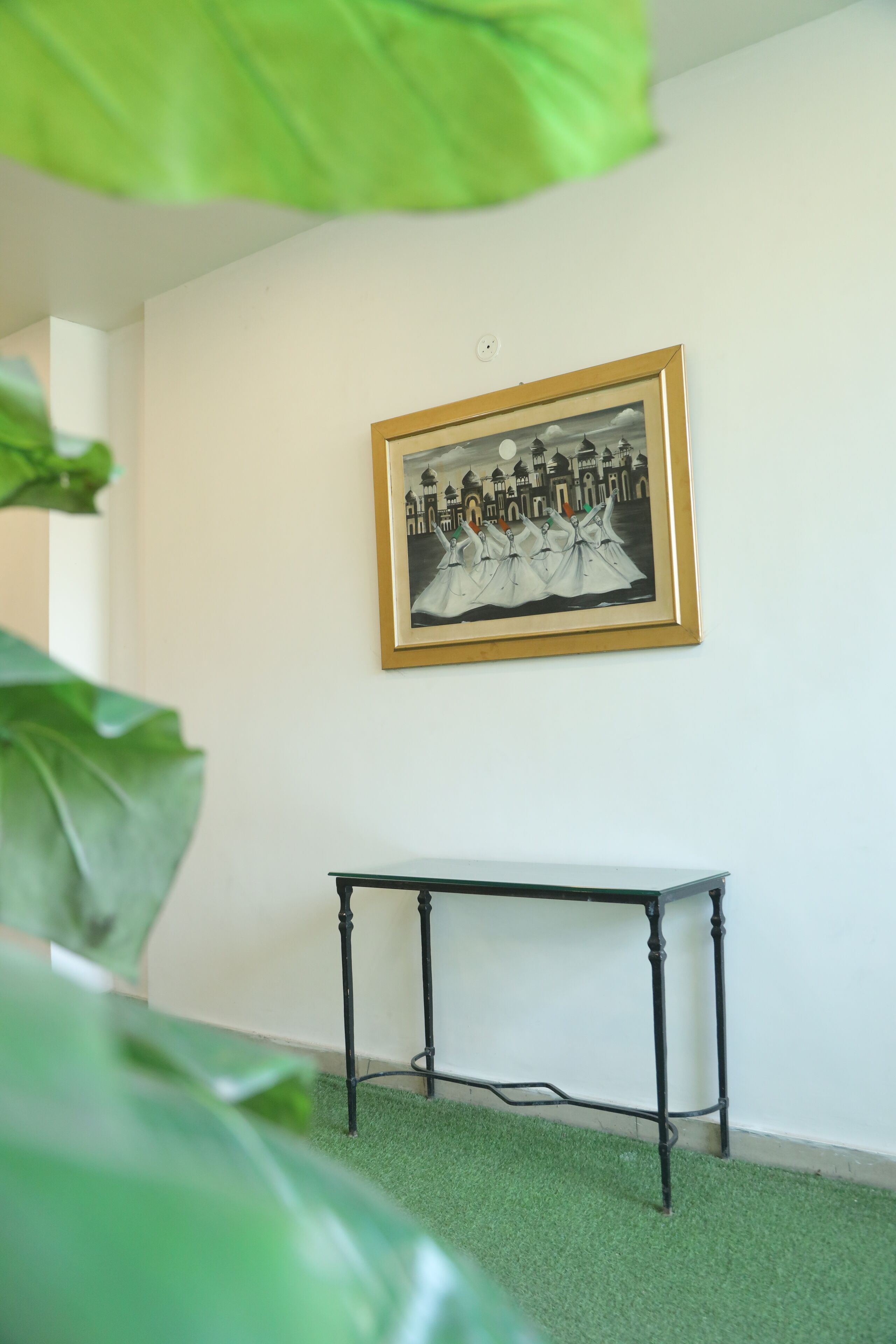 A room with a framed black and white photograph on the wall, a small table with metal legs, and green artificial grass on the floor.